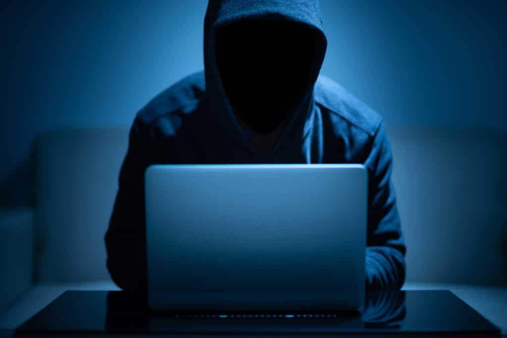 Hacker using laptop in dark room committing cybercrime against the cannabis Industry.